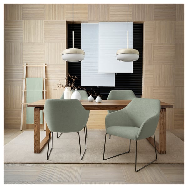 Salle à manger moderne avec des chaises vertes TOSSBERG, une table en bois et des suspensions contre un mur texturé.
