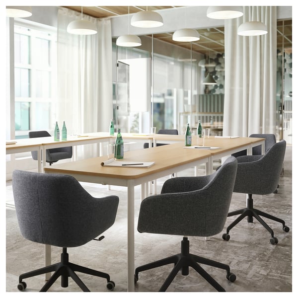 Salle de conférence moderne avec chaises pivotantes TOSSBERG en tissu gris, longue table en bois, bouteilles d’eau vertes et suspensions.