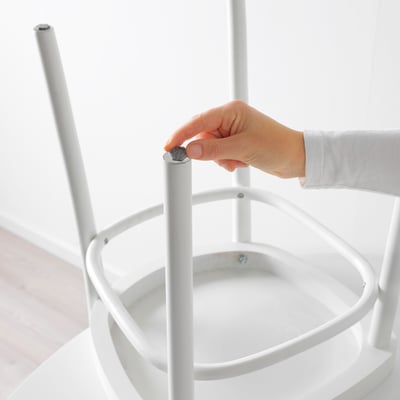 Une main fixe un petit tampon rond et autocollant à un pied de meuble, protégeant ainsi les sols des rayures.