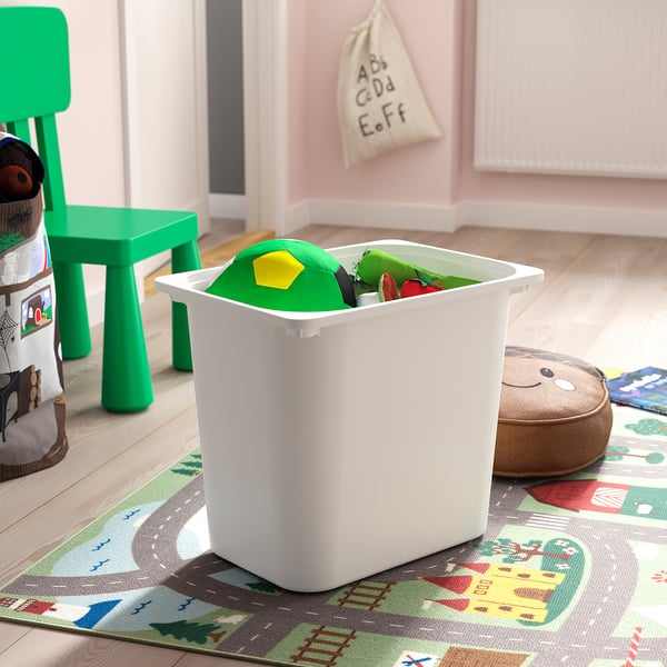 Bac de rangement en plastique blanc, rempli de jouets colorés, sur un tapis de jeu pour enfants avec une chaise verte à proximité.