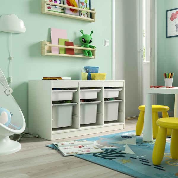 Salle de jeux avec unité de rangement TROFAST, vert clair, en bois, basse, cubes pour le rangement, près des chaises jaunes et de la porte ouverte.