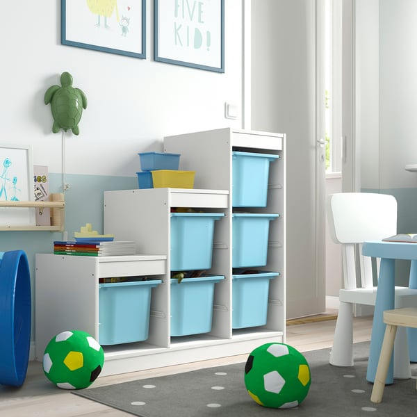 Chambre d’enfant avec rangement TROFAST, blanc, contenant des bacs en plastique bleus. Un espace ludique avec des jouets, des livres et des chaises.