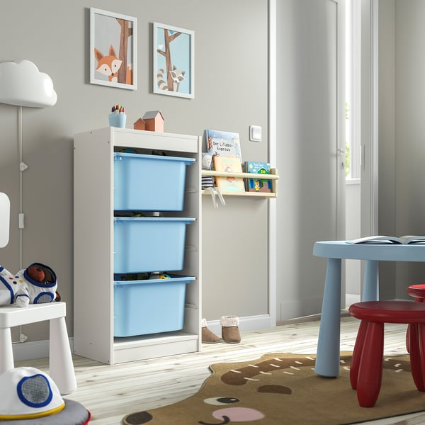 Chambre d’enfant avec rangement TROFAST, bacs bleus, estampes boisées, près d’une fenêtre.