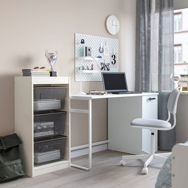 Espace d’étude moderne pour les enfants avec rangement TROFAST, bureau, ordinateur portable et papeterie. Les tiroirs en maille contiennent des livres et des trophées ; horloge sur le mur.