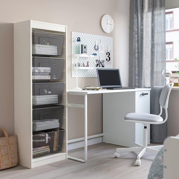 Une solution de rangement TROFAST blanche avec des boîtes en maille à gauche et un bureau avec une chaise d’ordinateur portable à droite, organisant efficacement un espace de travail.