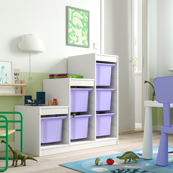 Rangement TROFAST blanc avec des bacs violets pour les jouets des enfants, des dinosaures verts et un tapis coloré dans le coin.