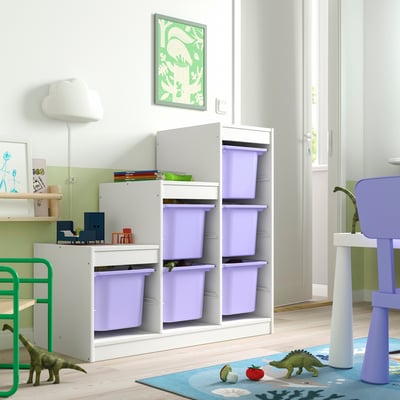 Rangement TROFAST blanc avec des bacs violets pour les jouets des enfants, des dinosaures verts et un tapis coloré dans le coin.