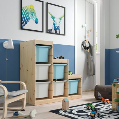 Rangement pour enfants : TROFAST, bois clair, bacs bleu clair/blanc, contient des jouets, placé contre le mur bleu, près de la chaise jouet.