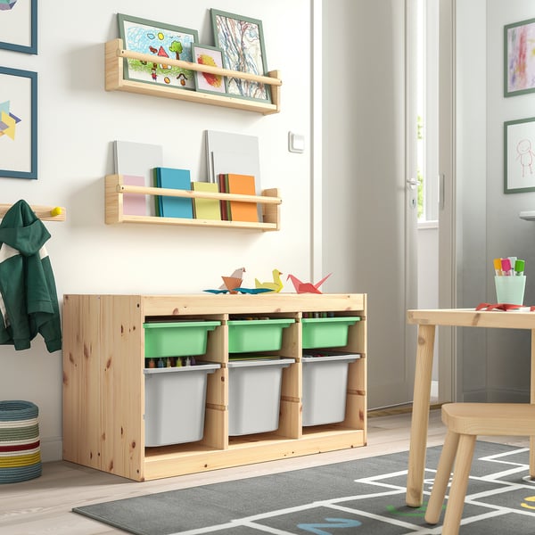 Chambre d’enfant avec rangement TROFAST : bacs en bois clair, verts et gris. Contient des jouets, des livres et des œuvres d’art. Espace lumineux et organisé.