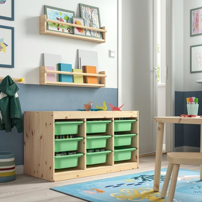 Chambre d’enfant avec unités de rangement vert clair TROFAST, cadre en bois et plusieurs compartiments ; étagères avec des livres et des œuvres d’art sur les murs.