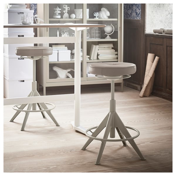 Deux tabourets gris clair avec des sièges rembourrés et des bases en métal pour une assise active.
