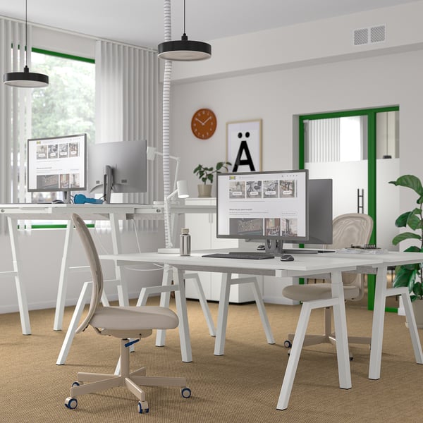 Bureau moderne avec bureau TROTTEN assis/debout, plusieurs écrans, chaises, plantes et décorations.