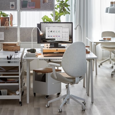 Un bureau blanc compact en trotte aux pieds angulaires, idéal pour les petits espaces, montré avec un moniteur et des fournitures de bureau.
