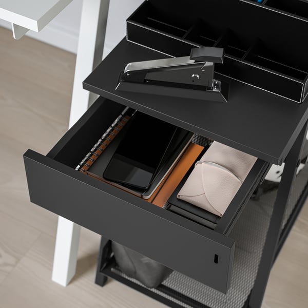 Unité de rangement TROTTEN noire avec tiroir ouvert révélant le portefeuille, le téléphone et les papiers. Verrouillable, idéal pour le rangement sécurisé d’un bureau ou d’une pièce.