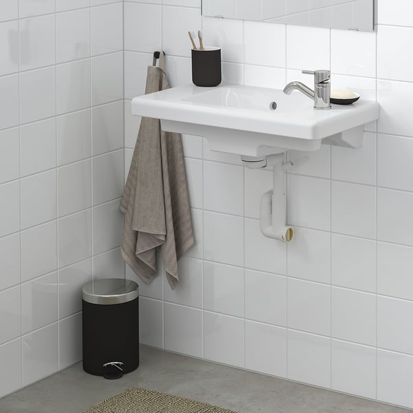 Lavabo mural moderne blanc avec serviette, porte-brosse à dents, porte-savon et robinet chromé. Fond carrelé blanc.
