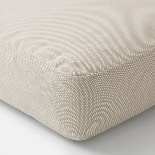 Gros plan d’un coussin beige de haute qualité. Tissu texturé, bords soigneusement cousus, parfait pour le confort en plein air.