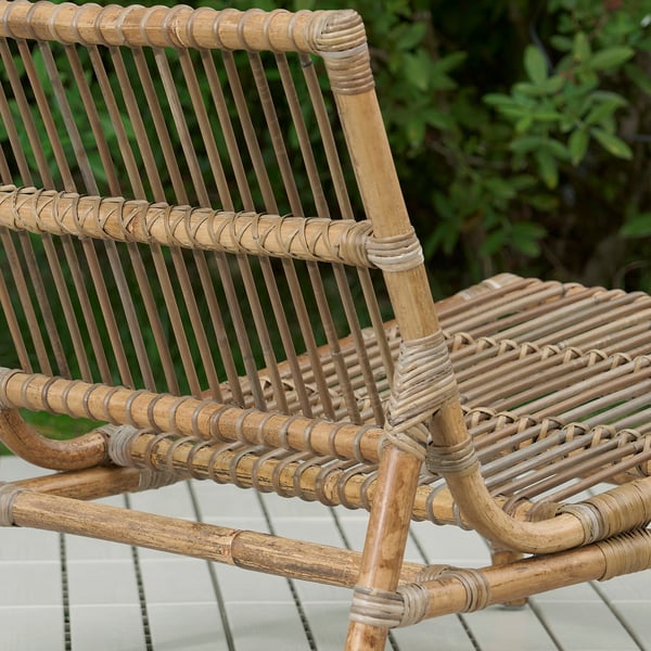 Chaise d’extérieur en rotin tressé, savamment fabriquée, exposée sur un patio carrelé, entourée de verdure.