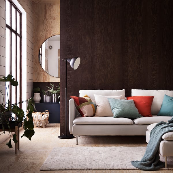 Salon moderne avec canapé blanc, oreillers colorés, textures en bois et un miroir circulaire. Un tapis d’inspiration berbère et des plantes d’intérieur ajoutent de la décoration.