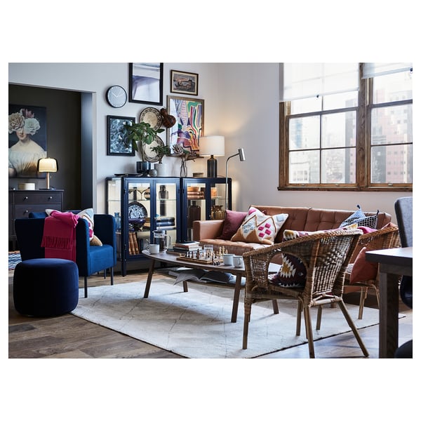 Salon moderne avec tapis beige, canapé marron, chaises en osier, accents bleus, vue sur la ville.