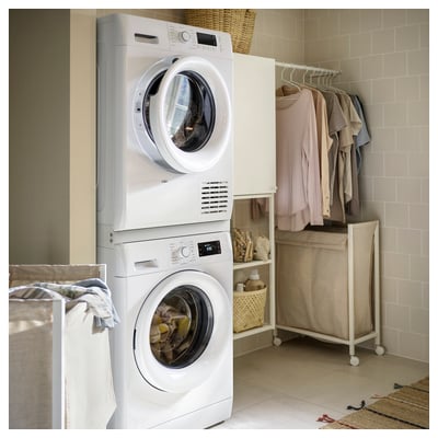 Une buanderie blanche avec des appareils TYKARP empilés. En bas : laveuse blanche, en haut : sèche-linge blanc. Les étagères environnantes contiennent des vêtements et des fournitures de lessive.