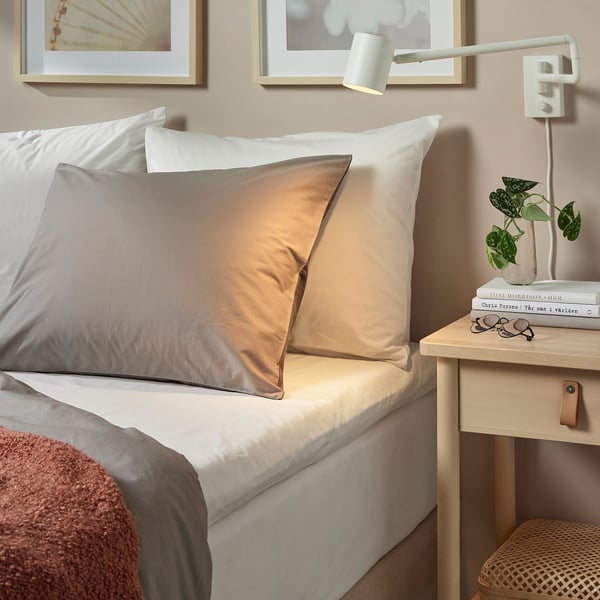 Lit avec draps blancs ULLVIDE, oreillers gris, petite table de chevet, lampe, plante et livres.