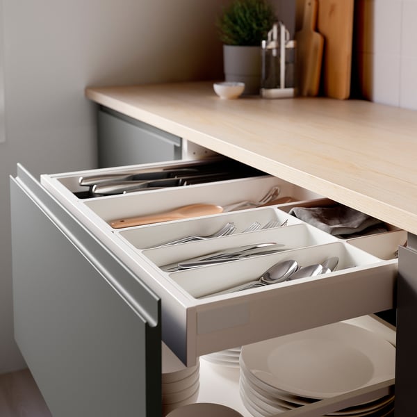 Tiroir de cuisine ouvert avec plateau à ustensiles organisé, y compris des fourchettes, des cuillères, des couteaux et une spatule en bois. Comptoir en bois de couleur claire visible au-dessus.