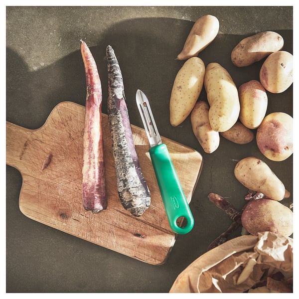 Planche à découper en bois avec deux légumes-racines, un éplucheur de pommes de terre vertes avec une lame en acier inoxydable. Pommes de terre et éplucheur prêts pour la préparation des aliments.
