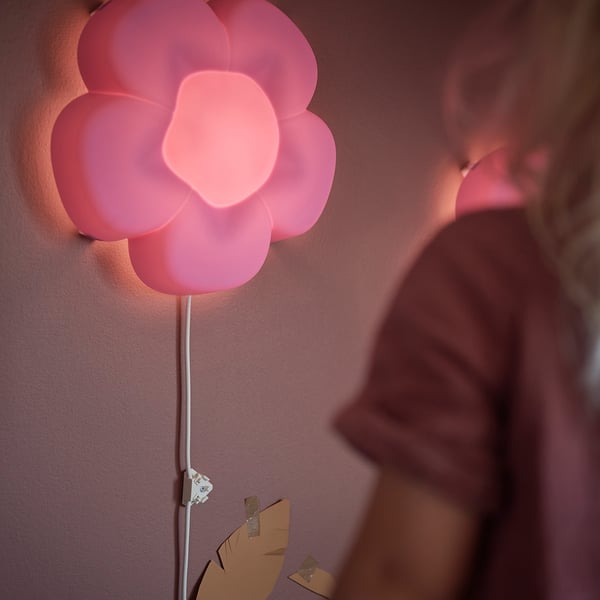 Applique murale en forme de fleur rose à la lumière douce, montée sur un mur.