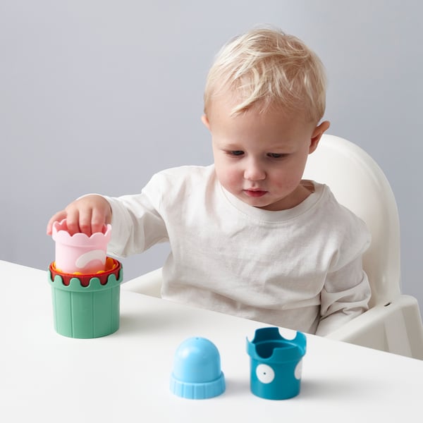 Un jeune enfant est assis dans une chaise haute et joue avec des tasses colorées qui s’empilent, explorant les formes et les couleurs.