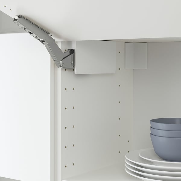 Charnière d’armoire blanche avec amortisseur intégré pour une fermeture lente et silencieuse de la porte ; bols et assiettes bleus sur l’étagère.