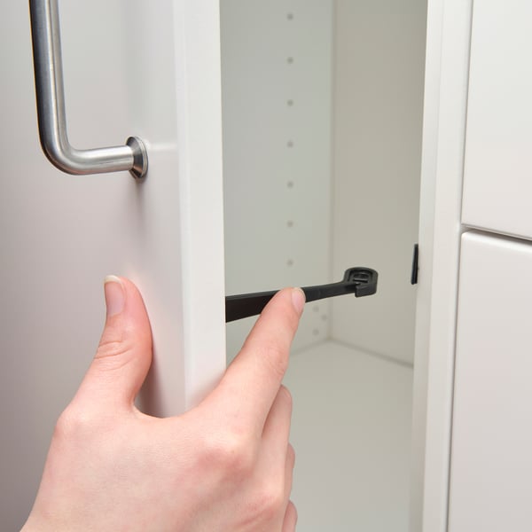 Une main fixe une serrure d’armoire noire à une armoire blanche, améliorant ainsi la sécurité des enfants.