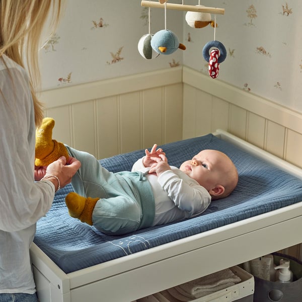 Femme mettant bébé dans un berceau avec une couverture pour chat et des jouets.
