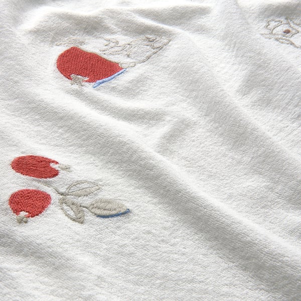 Couverture pour bébé brodée avec de doux détails rouges sur un tissu éponge blanc moelleux.