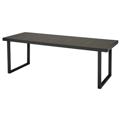Une table d’extérieur VÄRMANSÖ noire à l’aspect bois, fabriquée en aluminium et acier recyclés. Forme rectangulaire, design moderne.
