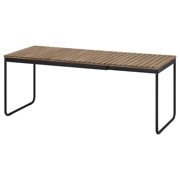 Table d’extérieur VÄSMAN, rectangulaire, bois brun clair, cadre en métal noir, design minimaliste.