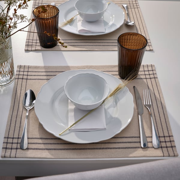 Deux tables avec de la vaisselle blanche, de l’argenterie, des tasses brunes et des sets de table beiges.