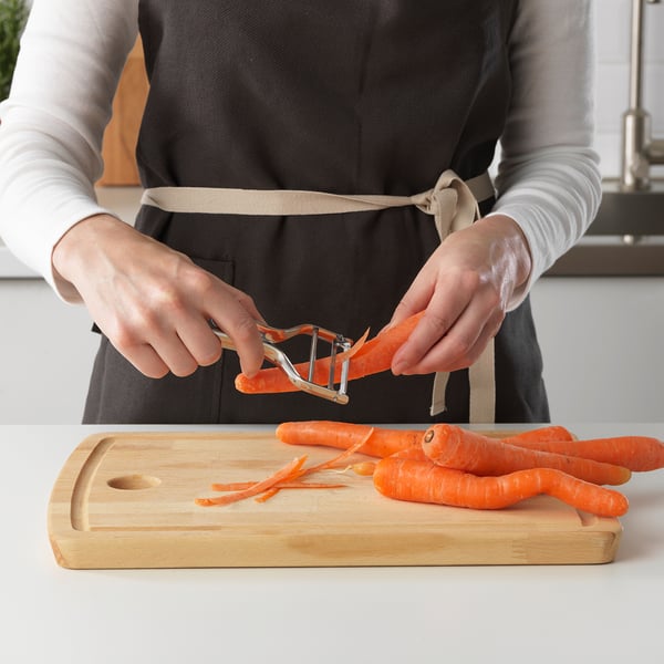 Personne épluchant des carottes à l’aide d’un économe sur une planche à découper en bois sur un comptoir de cuisine.