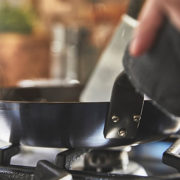 Personne tenant une casserole en métal par la poignée, probablement pour cuisiner.