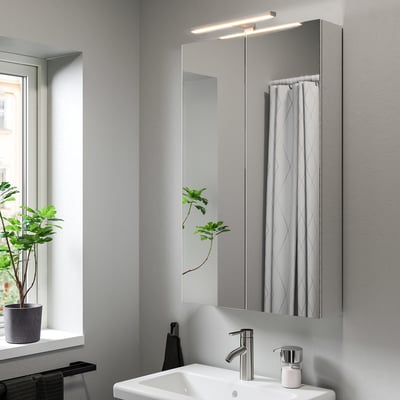 Salle de bain moderne avec lampe VÅTHULT au-dessus de l’évier, miroir et plante.