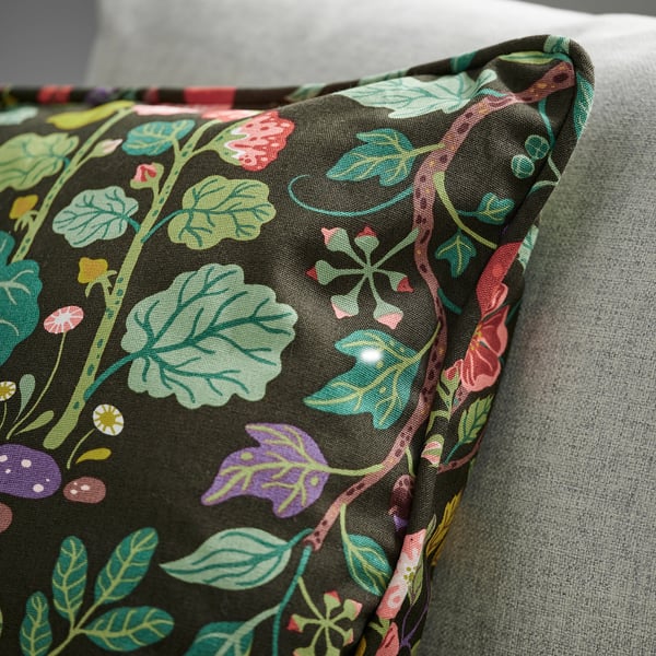 Coussin floral coloré sur canapé gris, mettant en valeur des motifs de feuilles complexes et des teintes vibrantes.