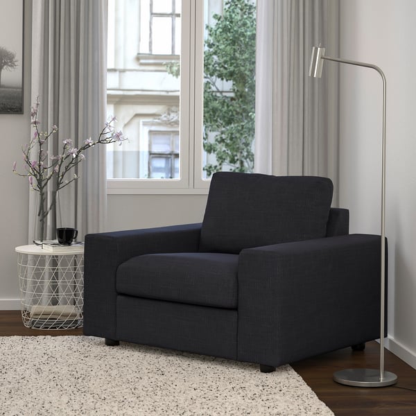 Fauteuil noir moderne à côté d’une grande lampe, sur un tapis léger.