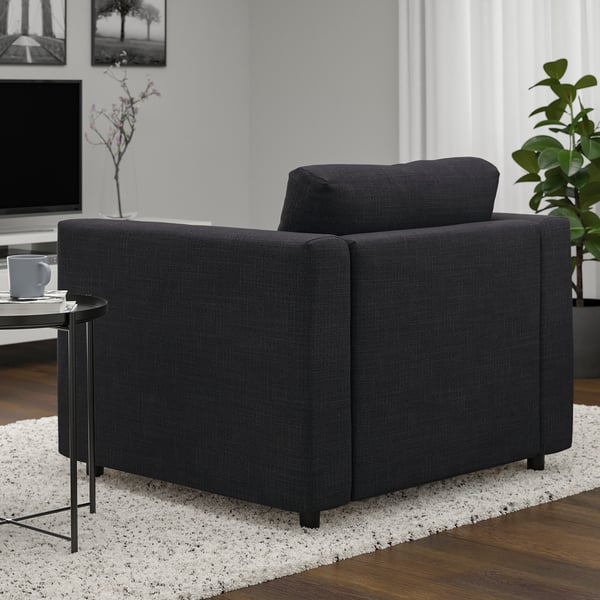 Fauteuil noir dans le salon, à côté de la table avec tasse, sur tapis, à côté de la plante en pot, avec télévision en arrière-plan.