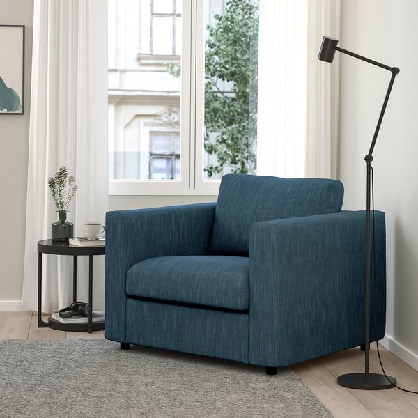 Salon moderne avec fauteuil VIMLE bleu, parquet en bois clair, tapis, lampadaire noir et petite table avec tasse à café et plante.