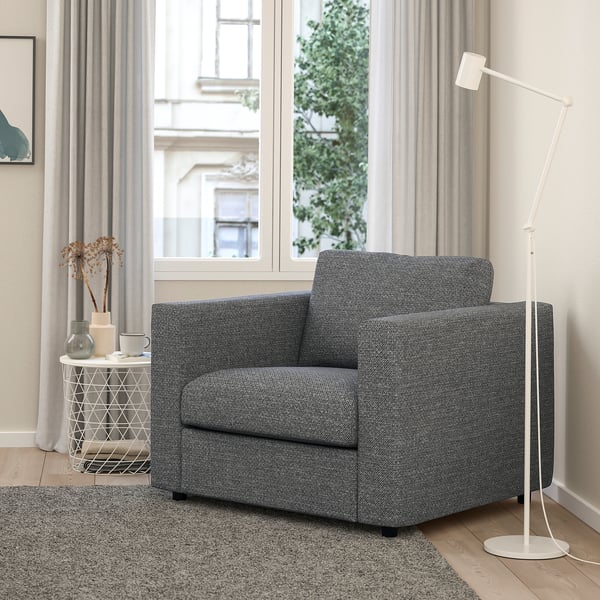 Chaise VIMLE grise moderne, de forme carrée. Placé entre la grande fenêtre et la lampe blanche, plus petit que la table d’appoint.