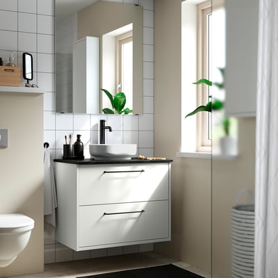 Salle de bain moderne avec un lavabo ovale en céramique VINDELÄLVEN blanc, robinet élégant, accents noirs, miroir et plante.