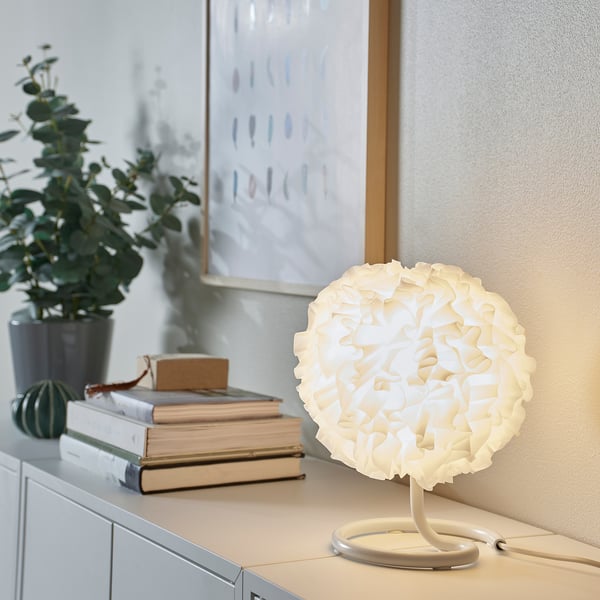 Lampe VINDKAST blanche écologique à côté de livres, petite, ronde, design moderne.