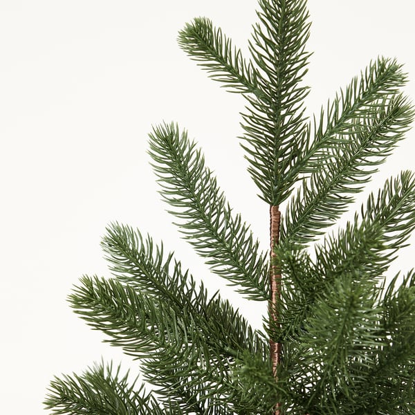 Gros plan d’une branche de pin artificielle, aiguilles vert vif, texture détaillée, fermement attaché à la tige brune.