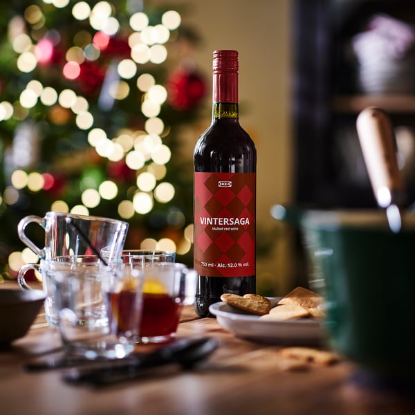 Bouteille de vin rouge chaud IKEA VINTERSAGA à côté de verres, de biscuits et de lumières de sapin de Noël.