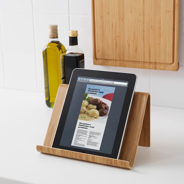 Une tablette affichant une recette dans un support en bambou sur un comptoir de cuisine. Bouteilles d’huile d’olive et de vinaigre en arrière-plan.