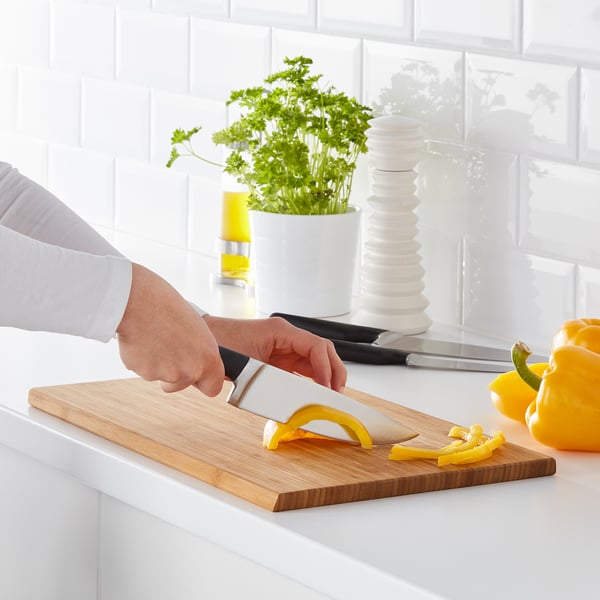 Personne coupant du poivron jaune sur une planche à découper en bois avec un couteau de cuisine. Set de couteaux conçu pour diverses tâches de cuisine.